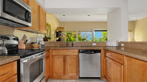 A kitchen with wooden cabinets, stainless steel appliances, and a view of greenery outside.