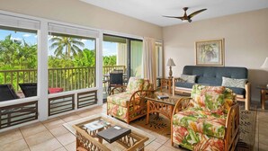 A room with a balcony, a sofa, two chairs, a table, and a ceiling fan.