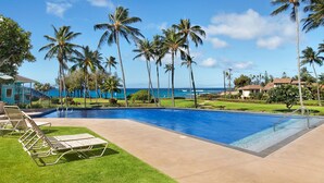 A swimming pool with lounge chairs, palm trees, and a view of the ocean.