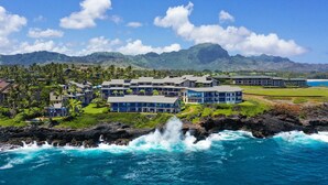 A coastal resort with multiple buildings, a rocky shoreline, and a view of distant mountains.