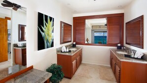 A bathroom with two sinks, wooden cabinets, a large mirror, and a view of the ocean.
