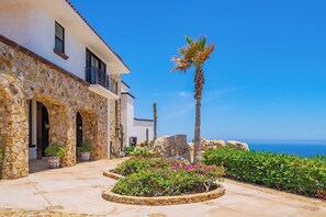 Ein Gebäude aus Stein mit einem Balkon, einer Palme und Blick auf das Meer.