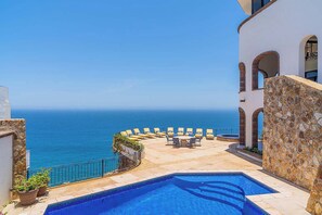 A pool area with a view of the sea, outdoor seating, and a stone wall. - Oceanfront Luxury 12k SqFt Med-Style Villa w/ Pool, Hot Tub & Ocean Views Cabo (Cabo San Lucas)