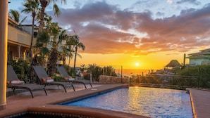 A pool area with lounge chairs and a sunset view.