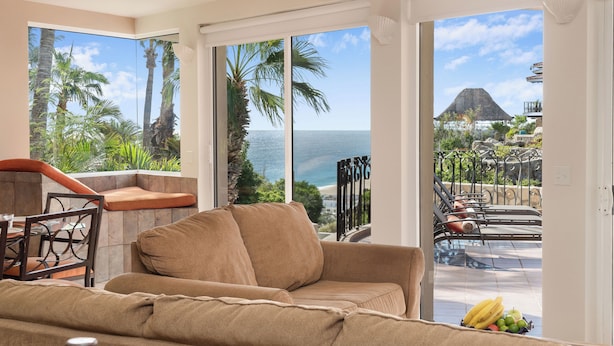 A living room with a large window overlooking a pool and a view of the ocean.