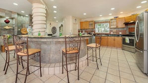 A modern kitchen with a central island, bar stools, wooden cabinets, and stainless steel appliances.