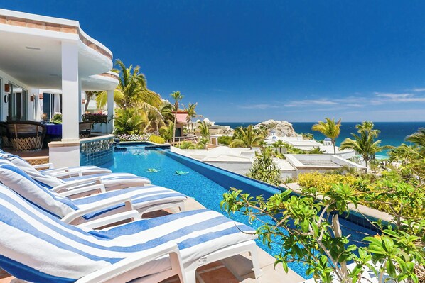 A pool area with lounge chairs and a view of the ocean.