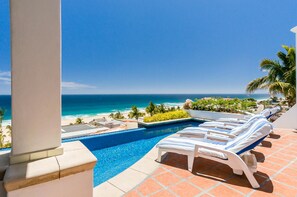 A pool area with lounge chairs and a view of the ocean.