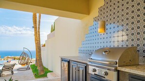 Una cocina al aire libre con una parrilla, un espacio de estar con una silla y vistas al océano.