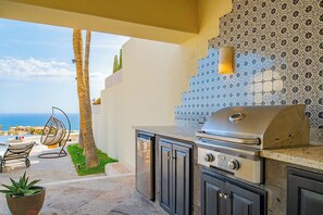 An outdoor kitchen with a grill, a seating area with a chair, and a view of the ocean.