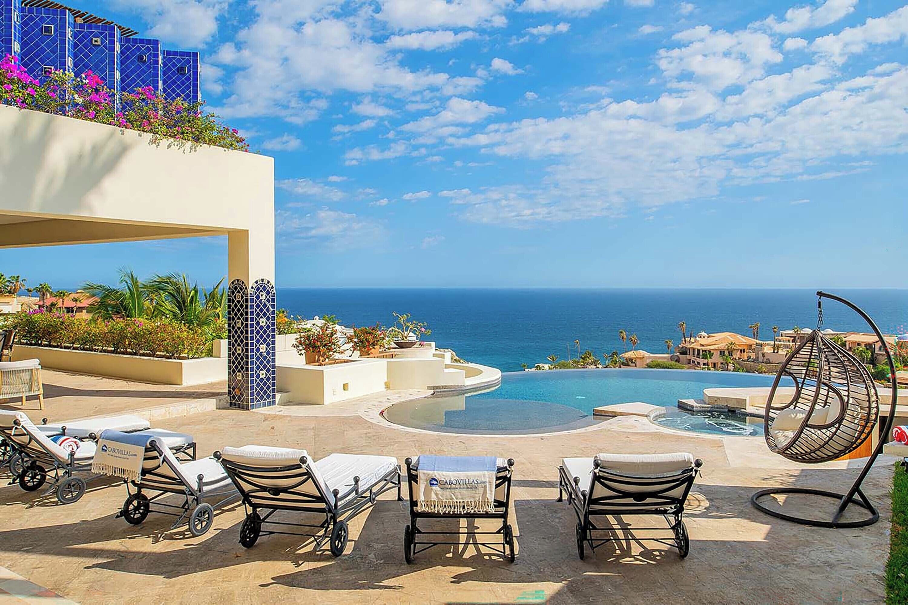 A poolside area with lounge chairs, a hanging chair, and a view of the ocean.