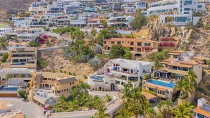 Zona residencial costera con arquitectura moderna, que incluye casas de techos planos y balcones, rodeada de palmeras y vegetación.