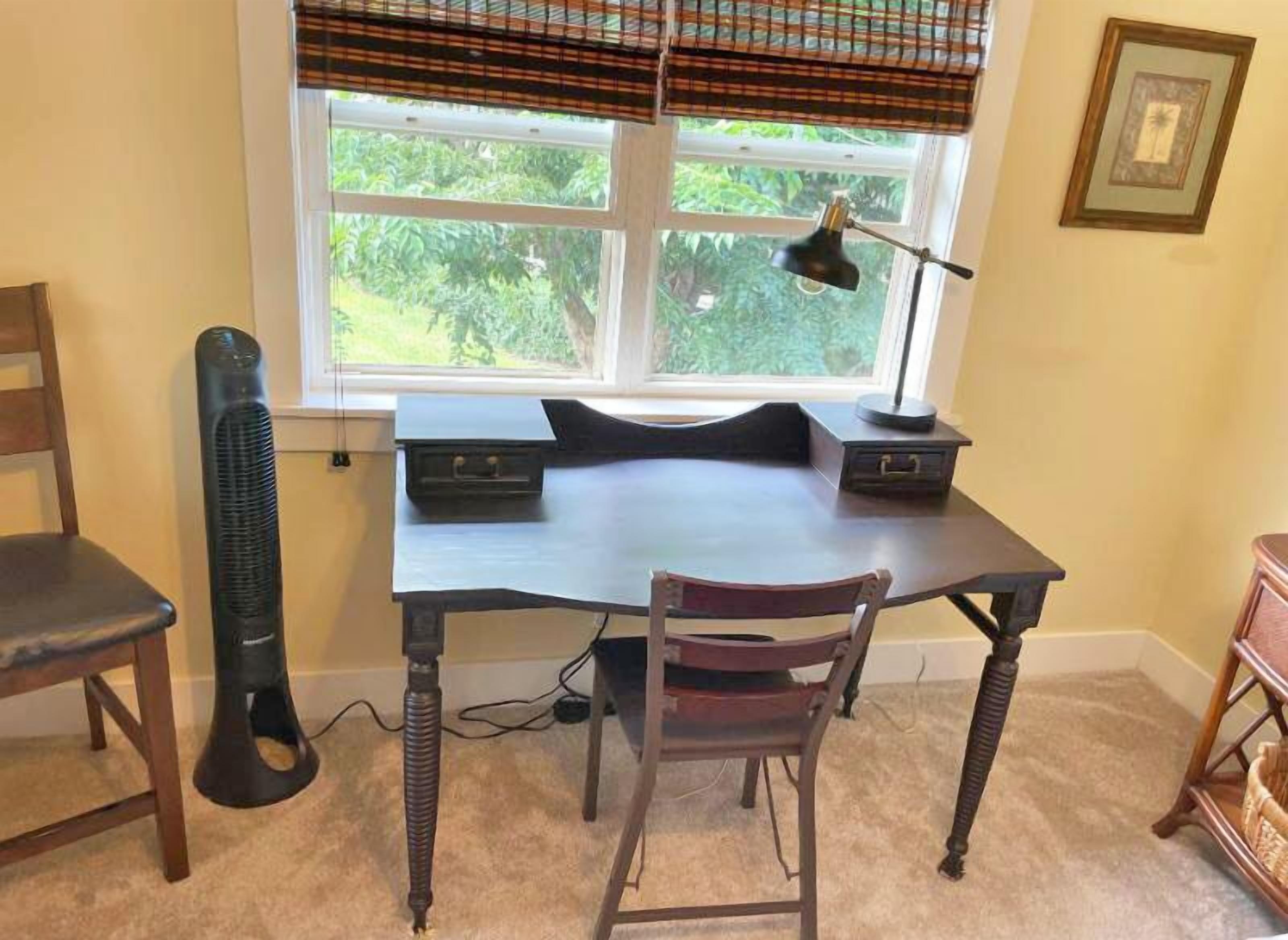 A study with a desk, two chairs, a lamp, and a window with blinds.