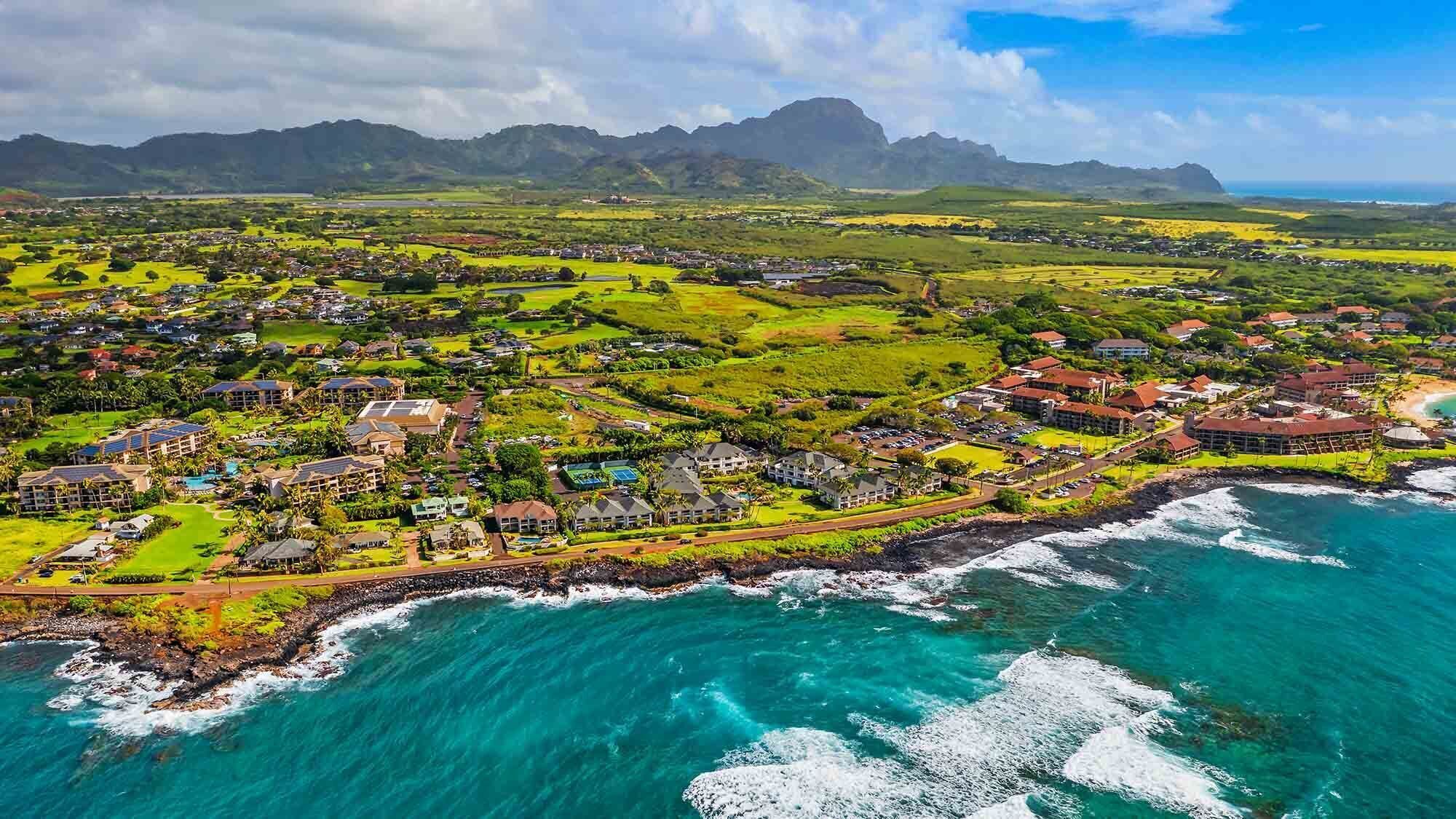 A coastal resort with multiple buildings, a beachfront, and a mountainous backdrop.
