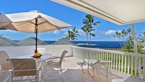A balcony with a table, chairs, and an umbrella overlooking the ocean.