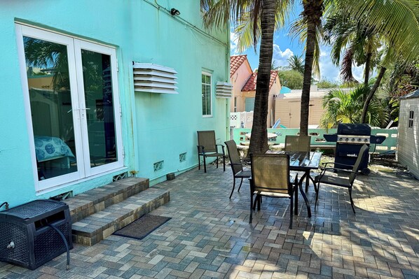 A patio with outdoor furniture, a grill, and a view of a building with a blue exterior.
