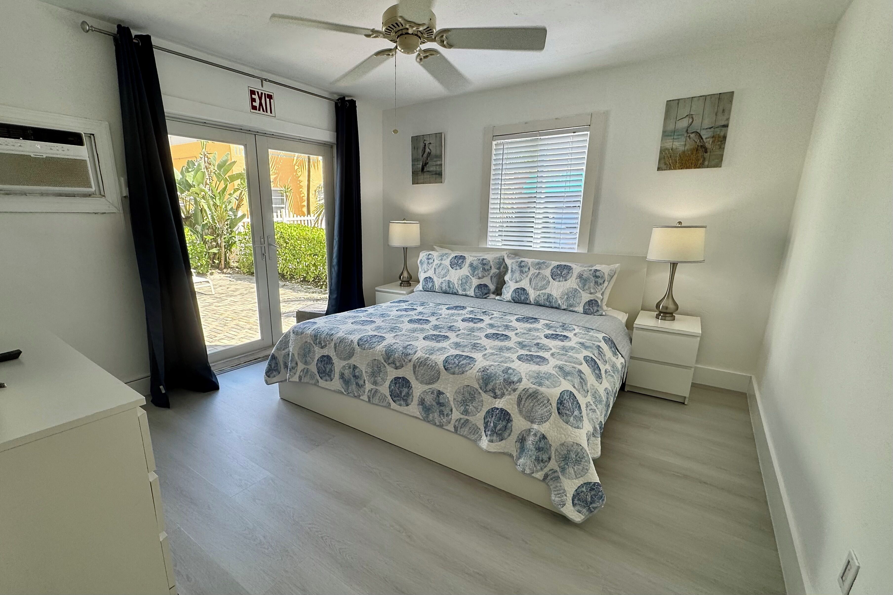 A bedroom with a bed, two bedside tables, a ceiling fan, and a view through a glass door.