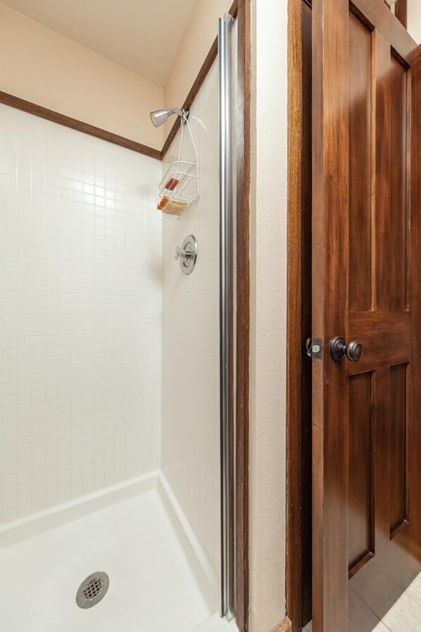 Une salle de bain avec une douche, une porte en bois et un mur carrelé.