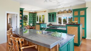 Una cocina con una isla central, armarios verdes y una zona de comedor con sillas de mimbre.
