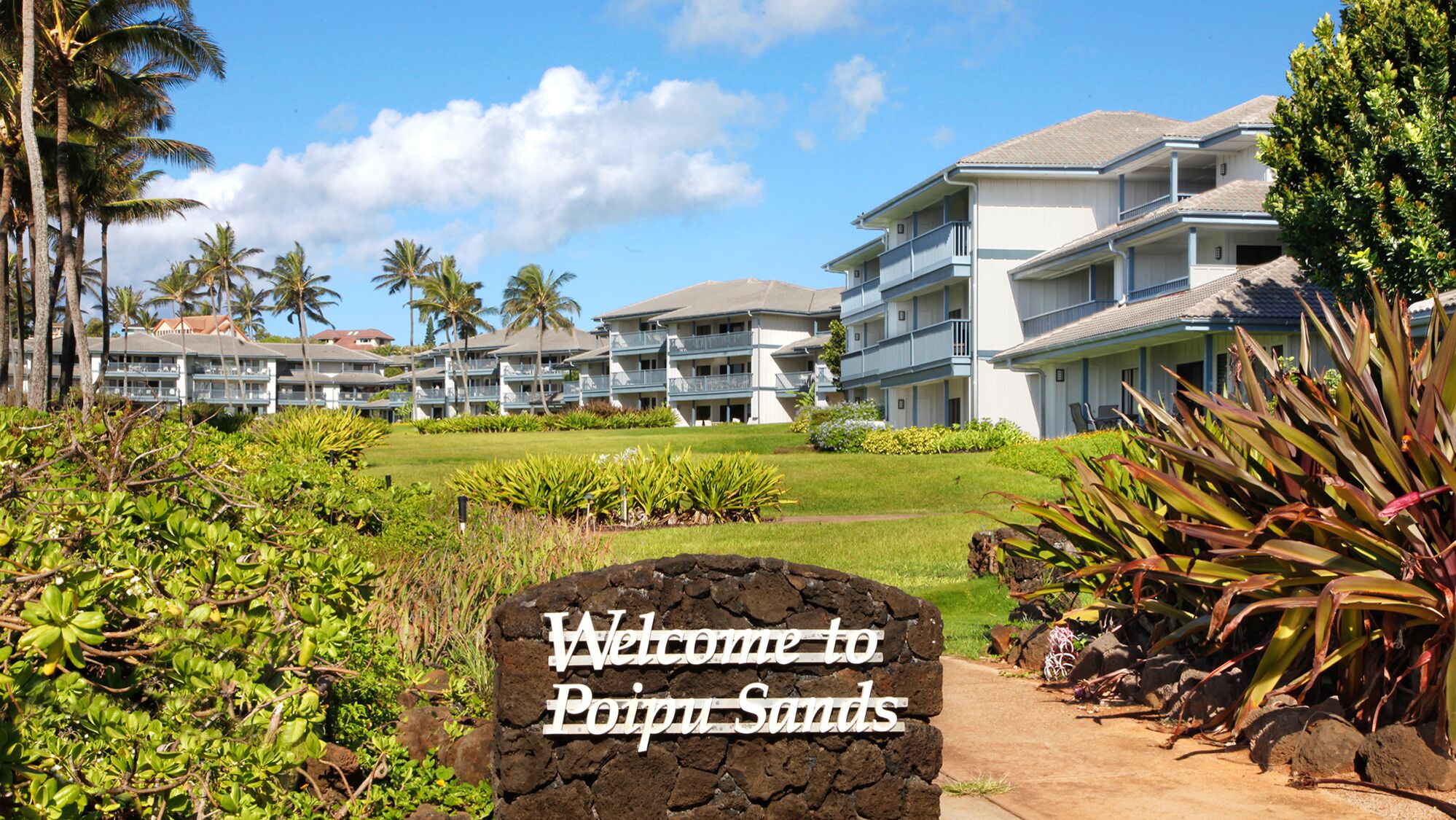 Entrada de un hotel con un letrero que dice "Welcome to Poipu Sands".