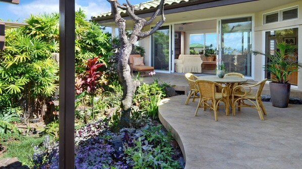 A patio with wicker furniture, a stone planter, and a variety of plants.