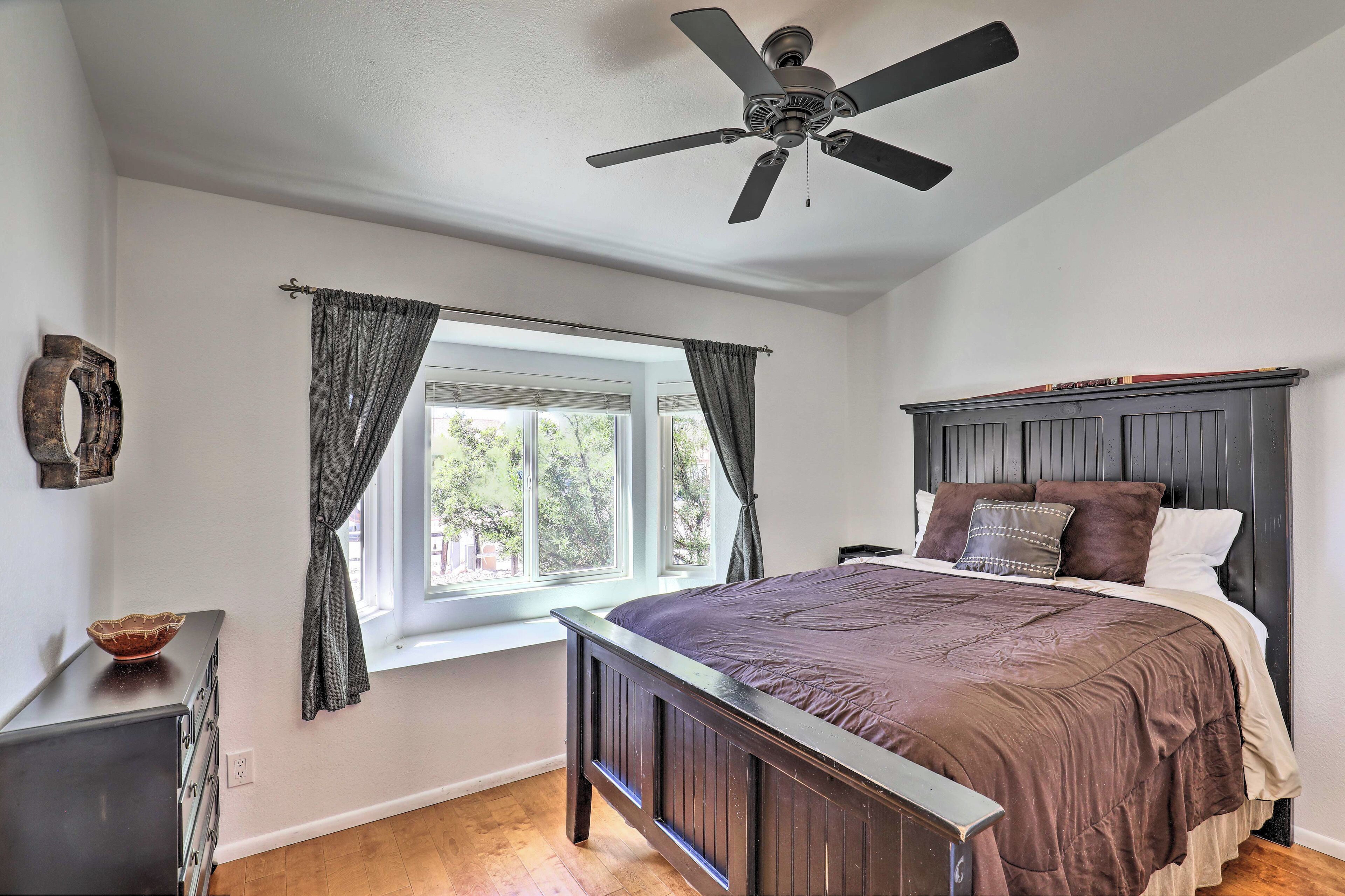 Une chambre à coucher avec un grand lit, un ventilateur de plafond, une fenêtre avec des rideaux et une commode.