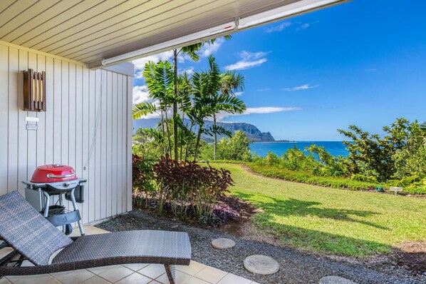 Un espace extérieur abrité comprenant un barbecue, un fauteuil de relaxation et une vue sur l’océan et les montagnes.