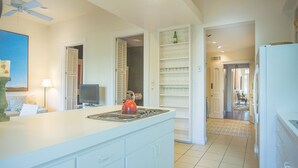 Una cocina con mostrador blanco, hervidor rojo y televisor.
