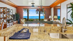 A modern living room with a view of the ocean, a kitchen with granite countertops, and a dining area. - Poipu Kapili 55 By Parrish Kauai- fabulous oceanfront & sunset views (Koloa)