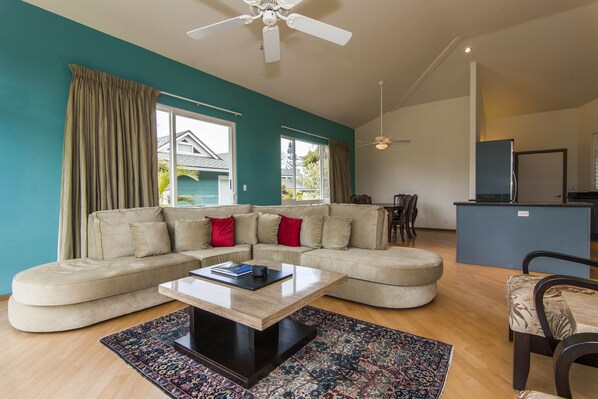 A living room with a sectional sofa, a coffee table, and a patterned rug. - Modern AC Home w/ Golf Course & Mountain Views! (Princeville)