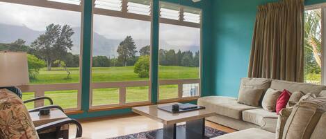 Una sala de estar con un ventanal grande, un ventilador de techo y vistas a un paisaje verde.