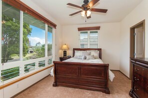 A bedroom with a large window, a ceiling fan, a wooden bed, and a dresser.