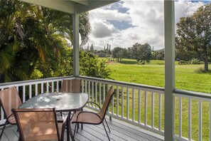 A covered outdoor area with a table and chairs, overlooking a grassy landscape with trees and a distant view of a house.