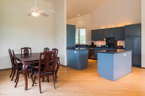 A modern kitchen with dark cabinets, a central island, and a dining area with wooden chairs and a table.