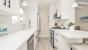 Una cocina moderna con armarios blancos, horno empotrado y encimera con hervidor y utensilios.