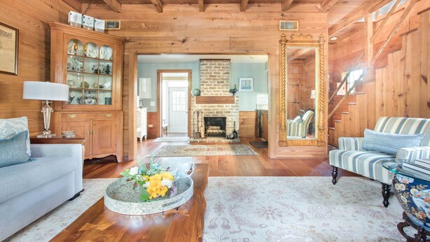 A wooden interior with a sofa, a striped armchair, a fireplace, and a dining area.