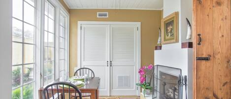 A dining area with a table set for two, a ceiling fan, a fireplace, and a wooden door.