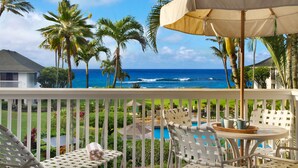 A balcony with a pool, white wicker furniture, and a view of the ocean.
