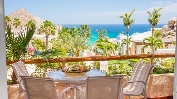 A balcony with a table and chairs, overlooking a beach and palm trees. - Pedregal Oceanview Villa w/ Pool, Hot Tub & Lush Landscaping (Cabo San Lucas)