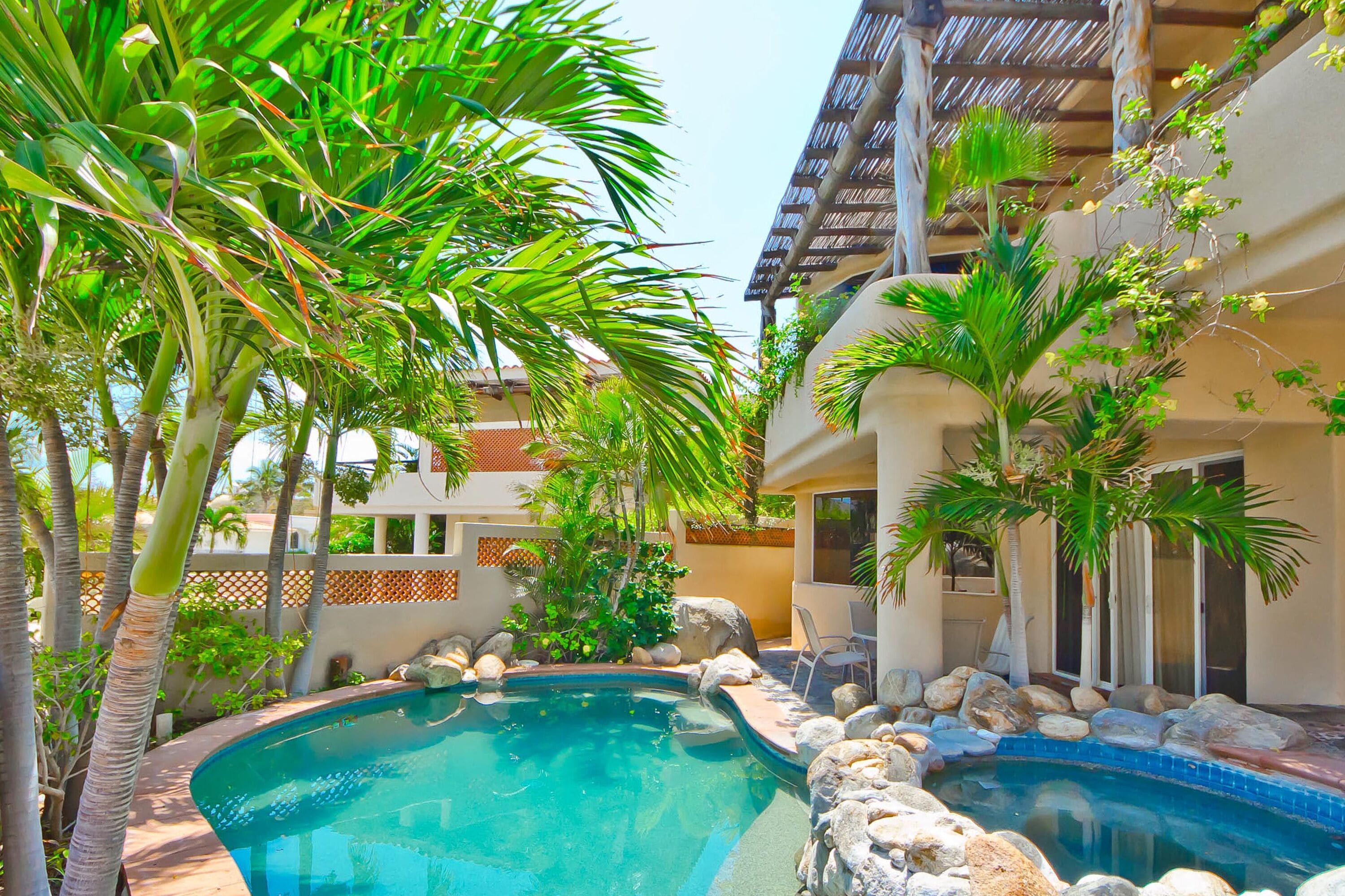 A swimming pool surrounded by rocks and palm trees, with a building in the background.