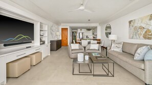 A modern living room with a flat-screen TV, a dining area, and a kitchen in the background.