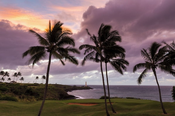 A golf course with palm trees and a lighthouse in the distance.