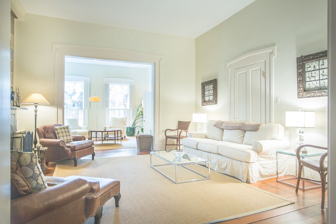 Un salon spacieux avec une grande fenêtre, un canapé blanc, un fauteuil en cuir marron et une table basse en verre.