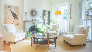 A living room with two white armchairs, a glass coffee table, a fireplace, and artwork on the walls.
