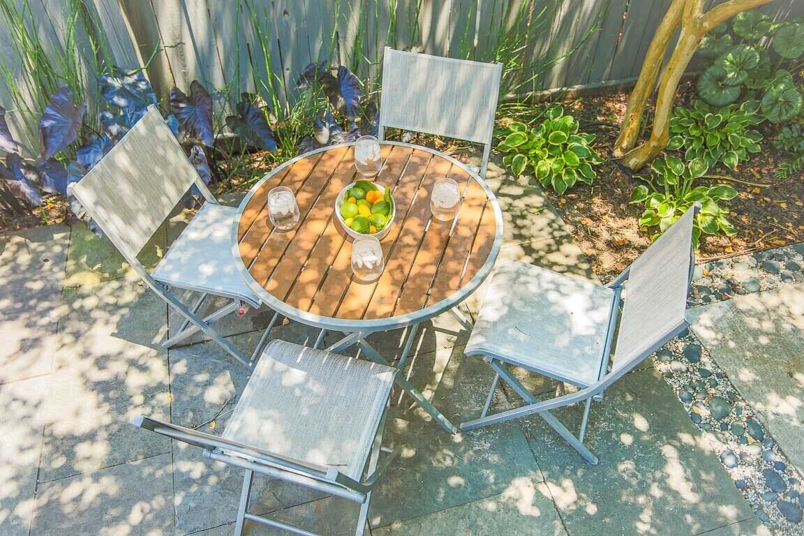 Una mesa redonda de madera con cuatro sillas de metal, rodeada por una valla de madera y plantas.