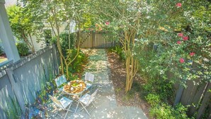 Un patio con mesa y sillas, rodeado por una valla de madera y abundante vegetación.