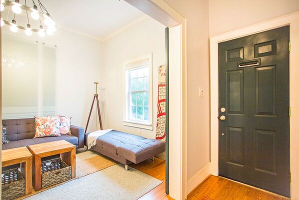 A room with a sofa, a small bed, a mirror, a door, and a window.