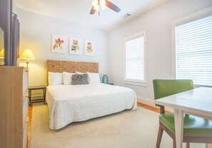 A bedroom with a bed, a desk, a chair, a lamp, and artwork on the wall.