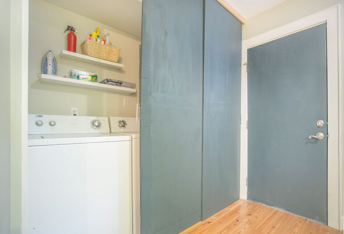 A laundry area with a washing machine, shelves with cleaning supplies, and a blue door.