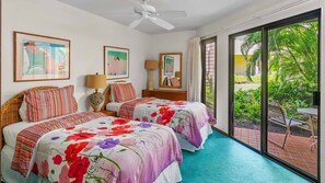 A hotel room with two beds, a ceiling fan, and a large sliding glass door leading to an outdoor area with a garden and a table.